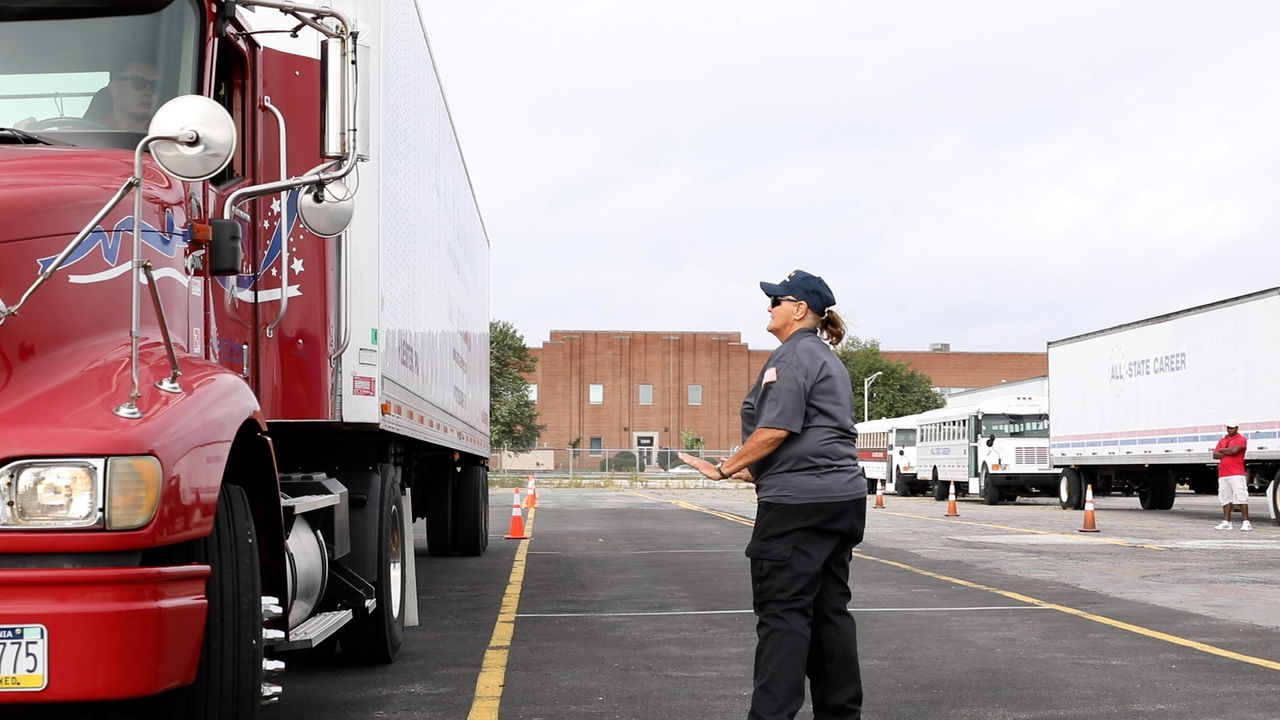 Female instructor guides red semi truck in parking lot
