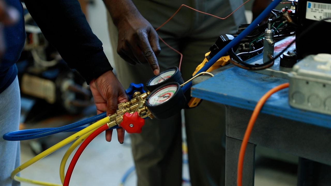 Technicians adjusting HVAC manifold gauge in workshop